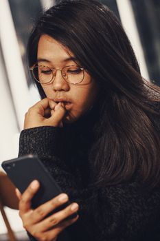 Asian woman in glasses using smartphone indoors in Bandung, Indonesia.