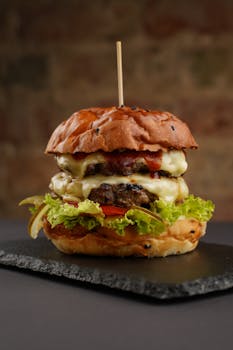 Mouthwatering gourmet burger with melted cheese, lettuce, and tomato on slate plate.