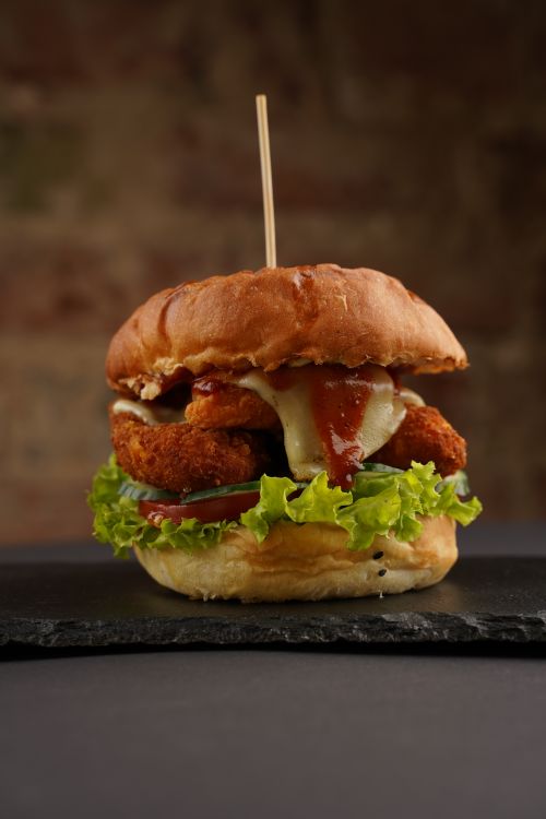 Free Close-up of a gourmet chicken burger with lettuce, cheese, and sauce on a slate plate. Stock Photo