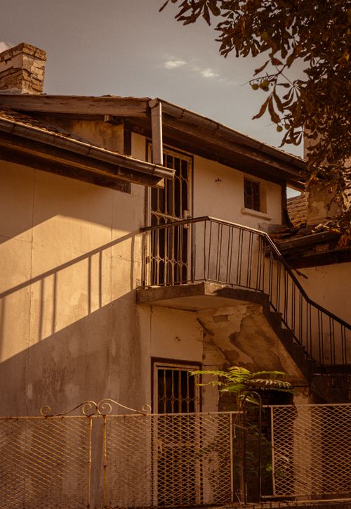 Free Aged residential building with a rustic balcony and steps, surrounded by shadows. Stock Photo
