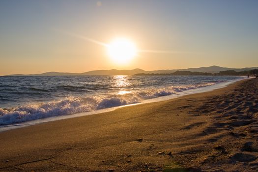 A sandy beach at sunset with gentle waves and a serene horizon view.
