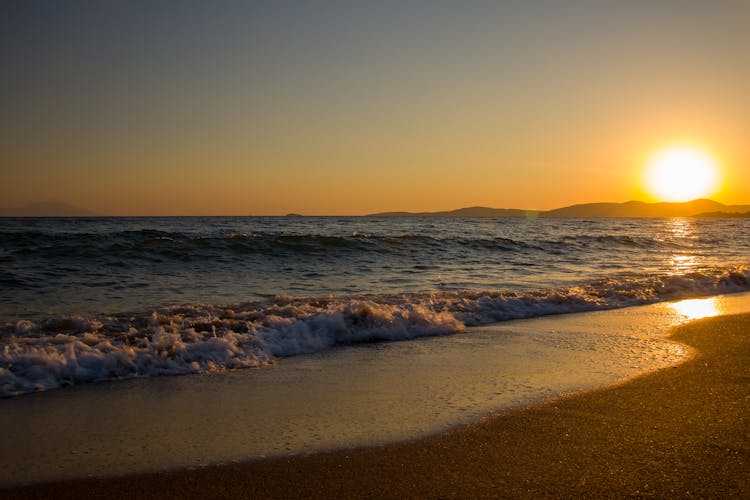 Rough Sea And Wet Sandy Beach With Yellow Sun Reflection