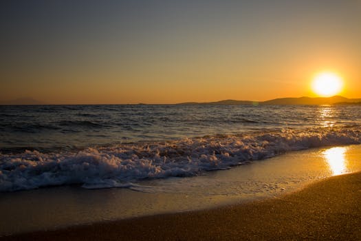 A serene sunset over the ocean with waves gently crashing on a sandy beach.