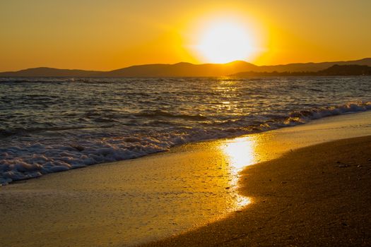 Golden sunset over the ocean, waves gently hitting the sandy shore. Peaceful and picturesque.