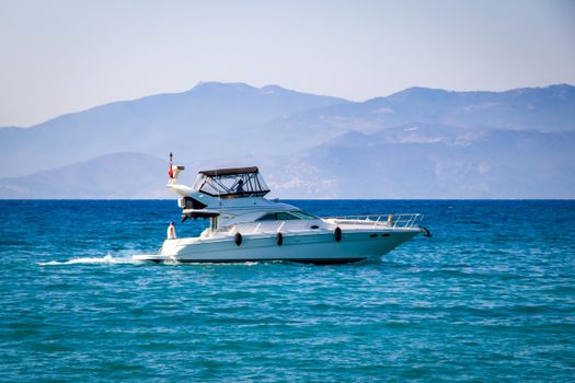 Elegant yacht sailing on calm blue ocean with a scenic mountain backdrop.