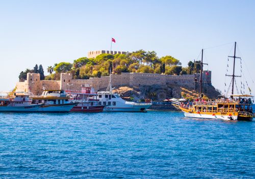 Scenic view of a coastal castle with boats in Kusadasi, Turkey on a clear day.
