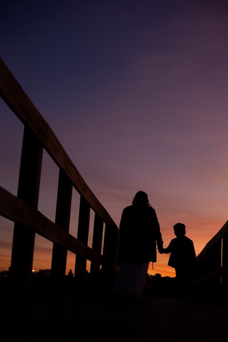 Silhouette Of Mother And Child Walking On A Bridge