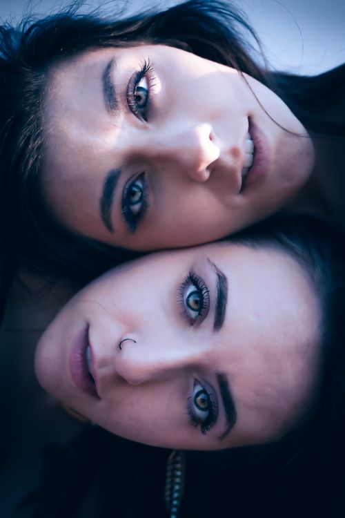 Free Captivating close-up portrait of two young women with striking green eyes and dark hair, in a serene embrace. Stock Photo