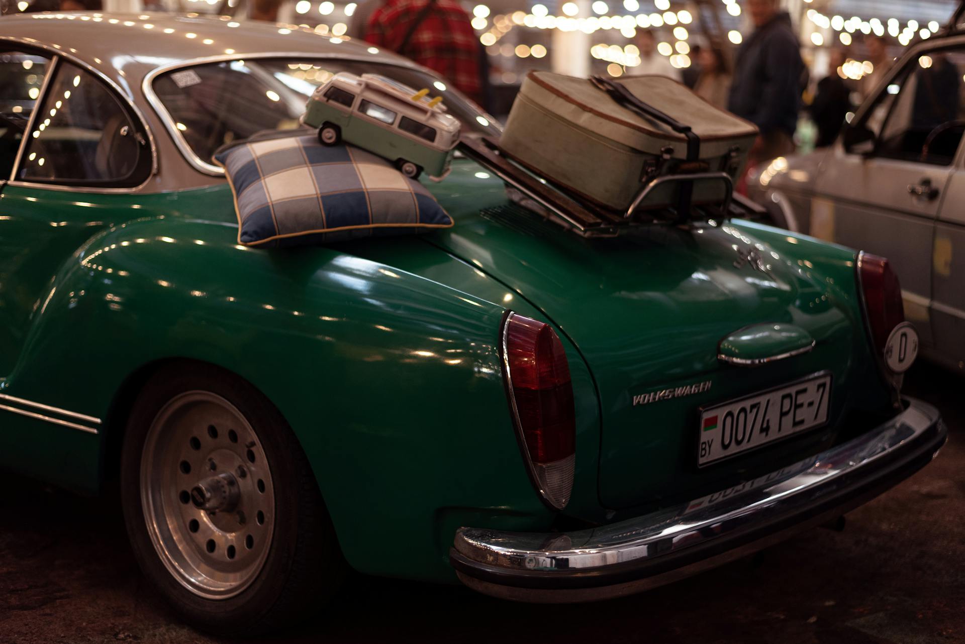 A classic green Volkswagen with luggage atop, showcased during a night car exhibition with vibrant lighting.