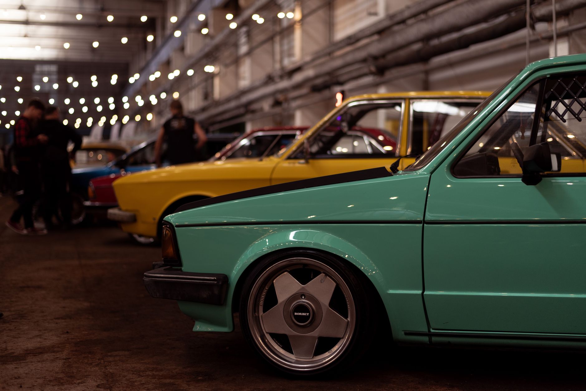 A vibrant indoor exhibition showcasing retro cars in various colors under warm lights.
