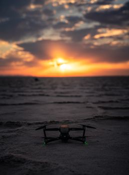 A drone sits on a sandy beach under a vibrant sunset, creating a serene and modern atmosphere.