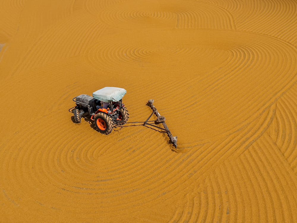 A Tractor with Plough Ploughing Brown Sand