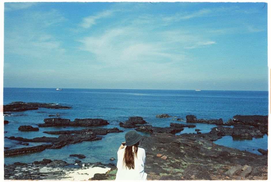 A woman in a hat enjoying the scenic view of a rocky seaside under a bright blue sky.