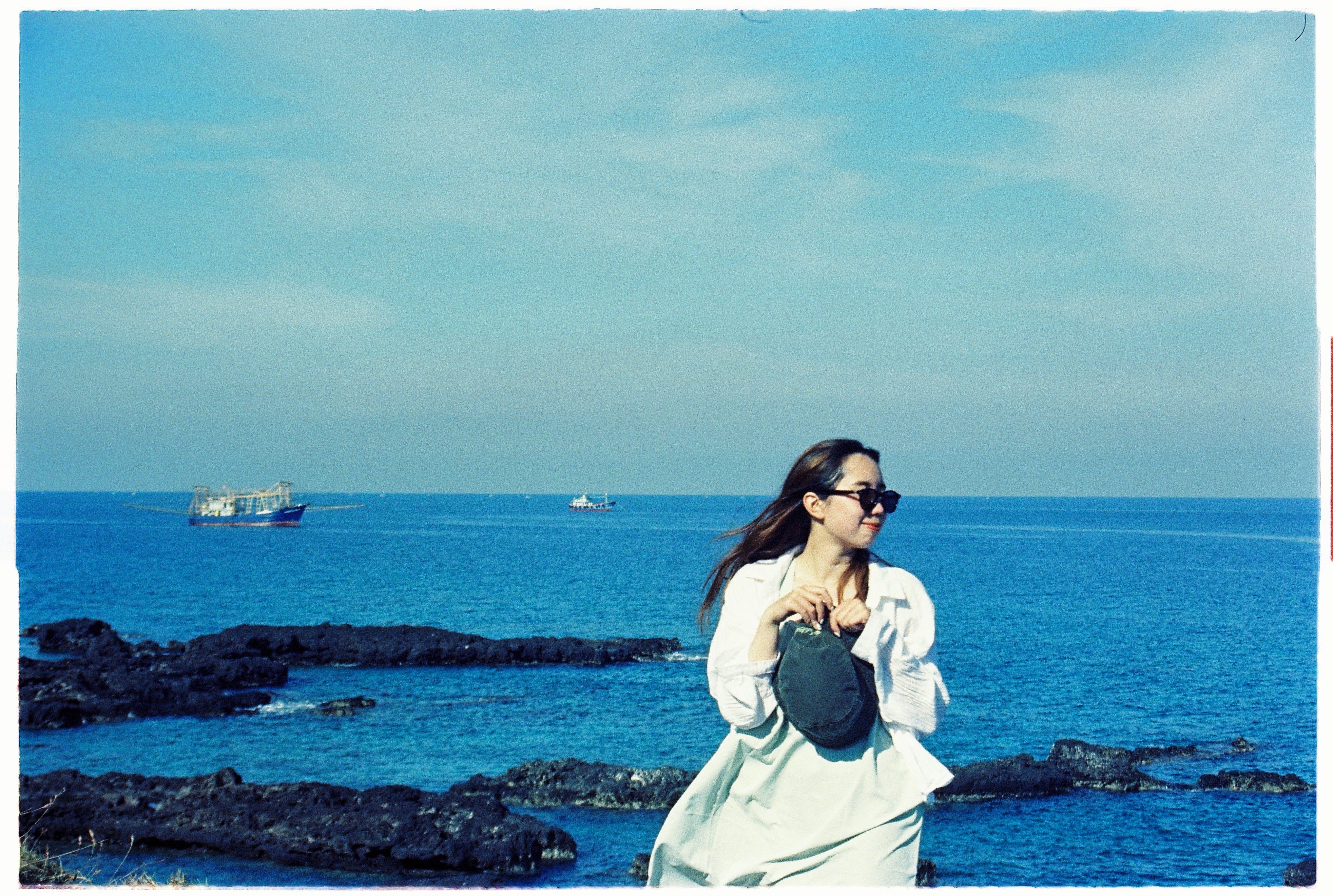 A woman wearing sunglasses gazes at the sea on a sunny beach day, exuding relaxation.
