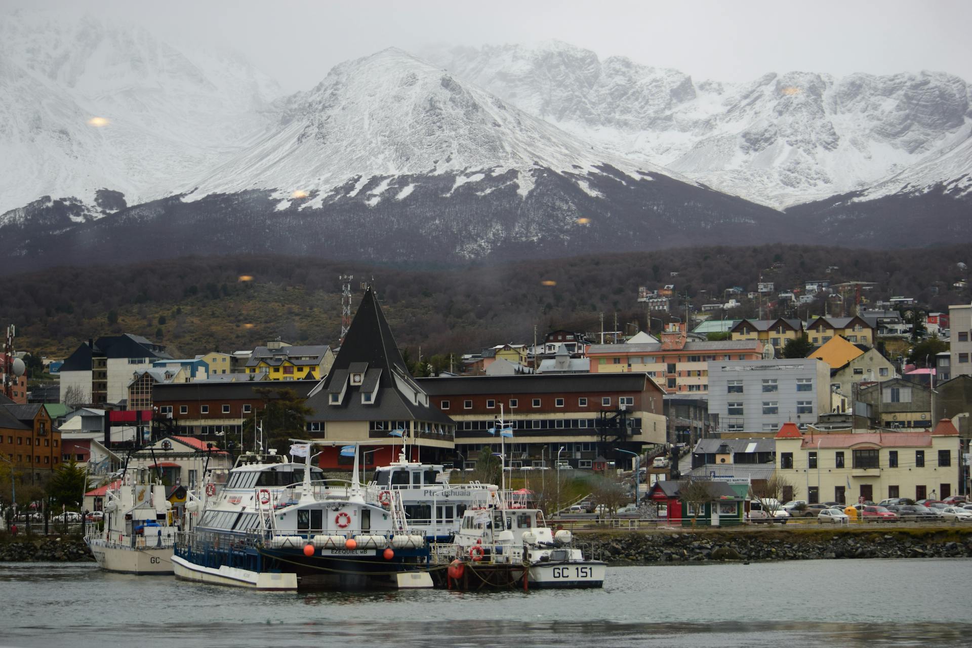 A scenic view of Ushuaia port in Argentina with boats and snow-capped mountains in the background.