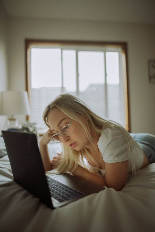 Free Young blonde woman using a laptop in a cozy bedroom setting, relaxed and focused. Stock Photo