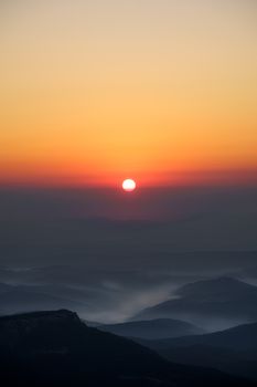 A tranquil sunrise casts warm hues over the misty Bosnian mountain range.
