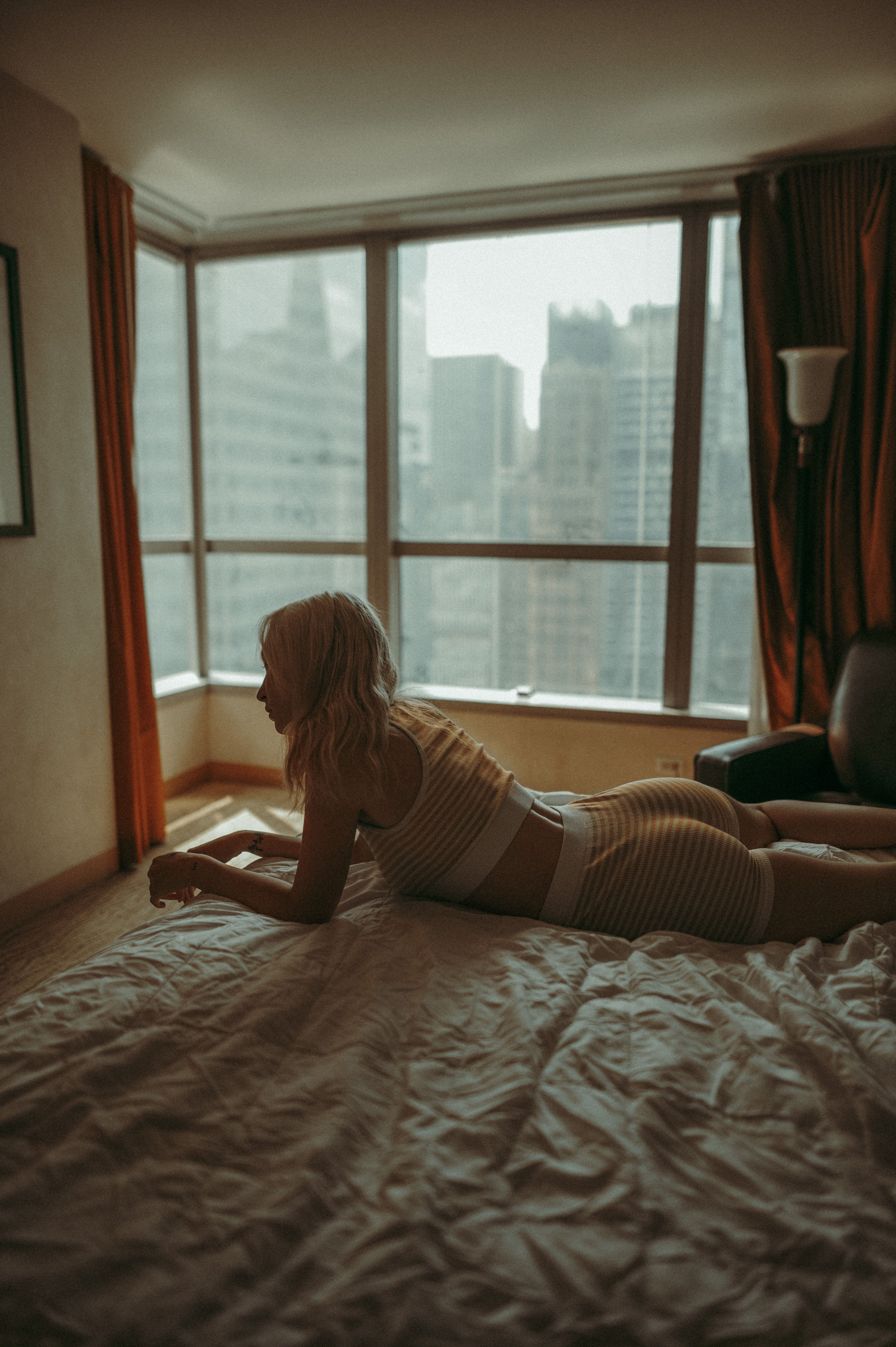 Young woman lying on a bed with a cityscape view in a modern urban apartment.
