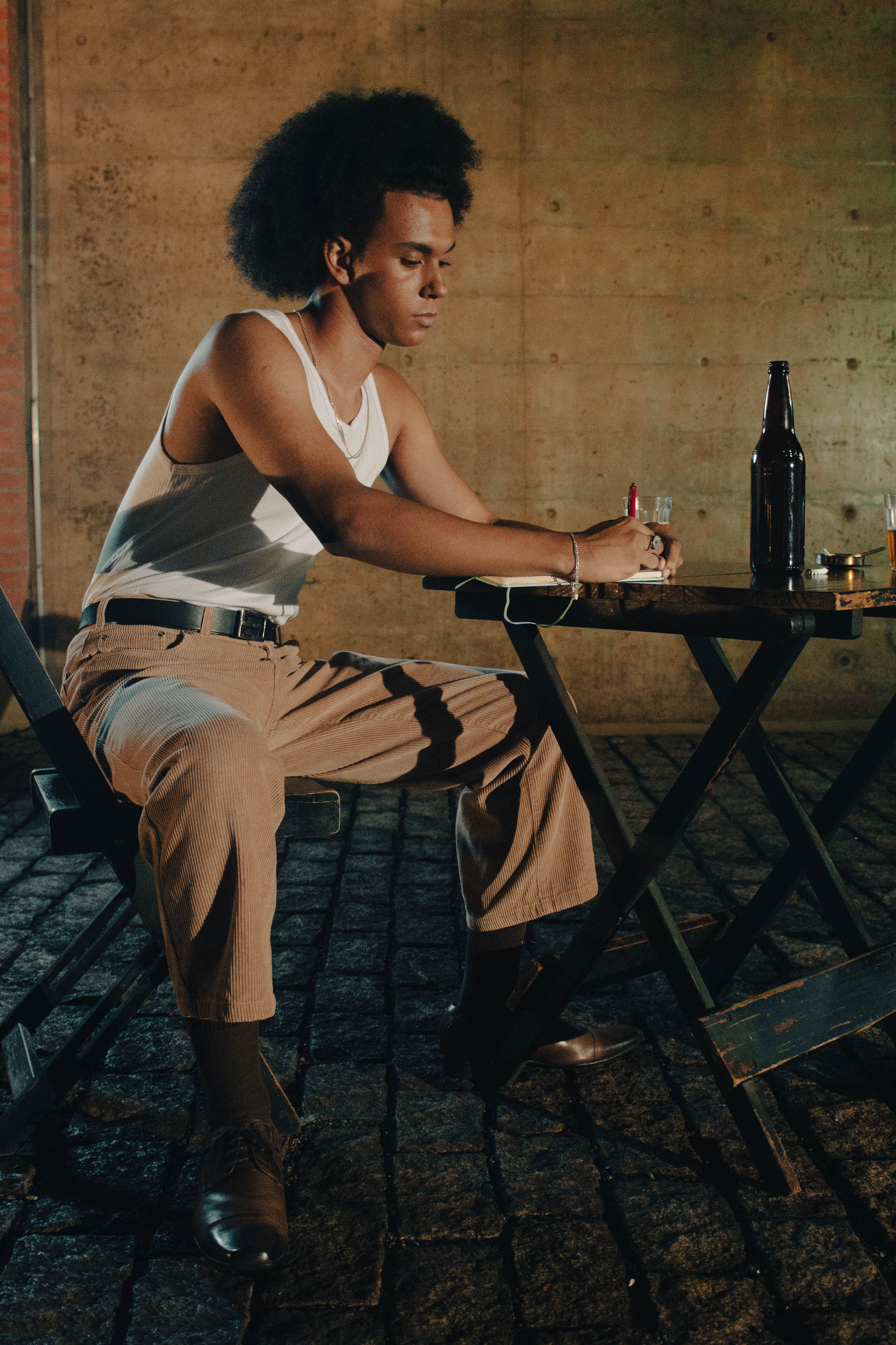 A thoughtful man sitting at an outdoor table with pen and paper, capturing inspiration in the evening light.