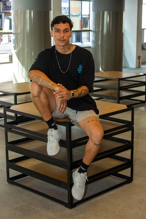 A Man in Black Shirt and White Sneakers Sitting on the Table