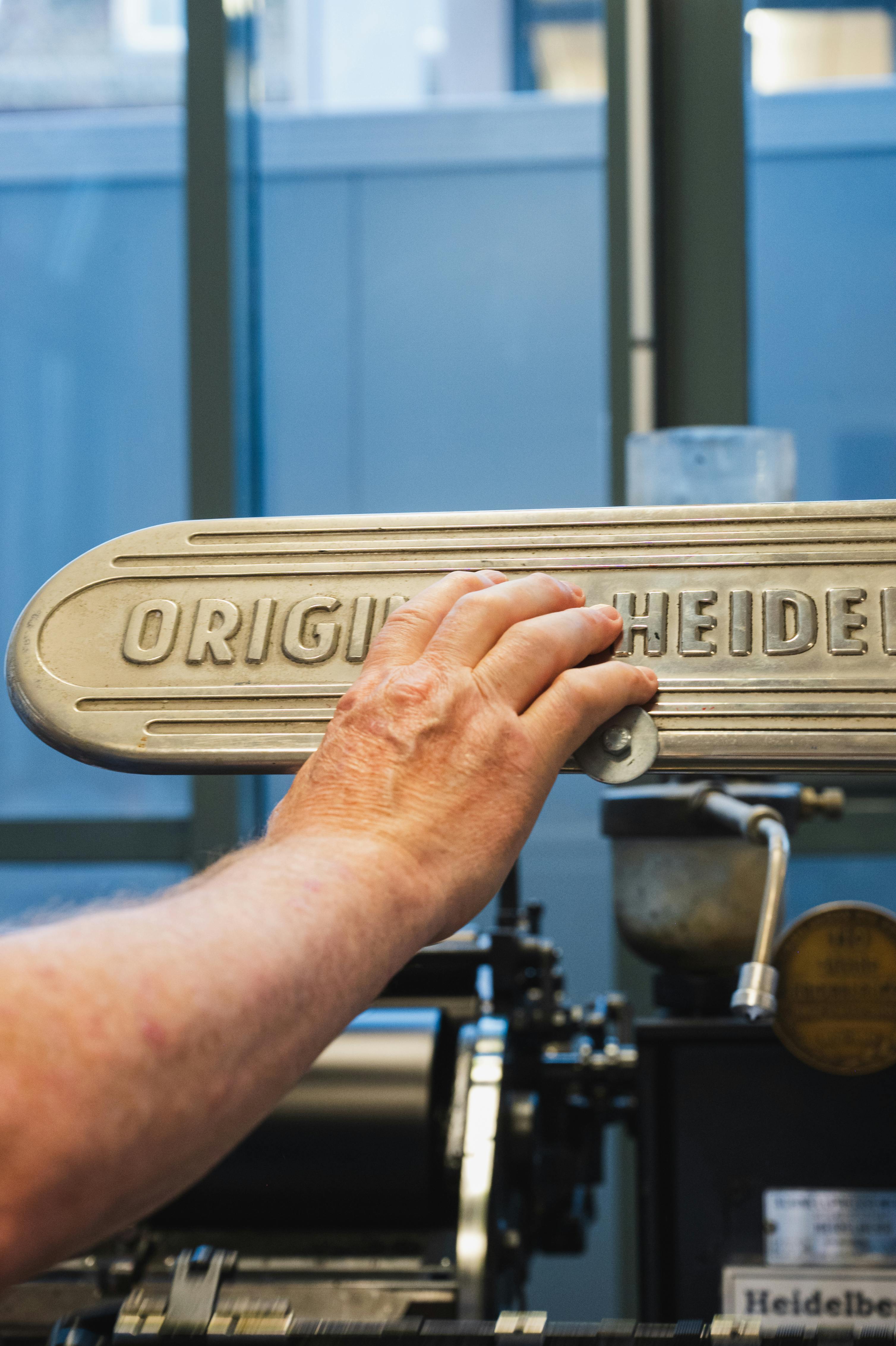 Detailed view of a hand operating a vintage Heidelberg printing press in Spira museum.