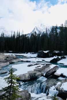 Scenic winter view of a snowy river in Banff National Park, Alberta, Canada, surrounded by snow-capped mountains and pine trees.