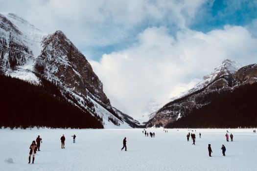 People enjoying winter activities on a frozen lake in Banff, with stunning snow-covered mountain scenery.
