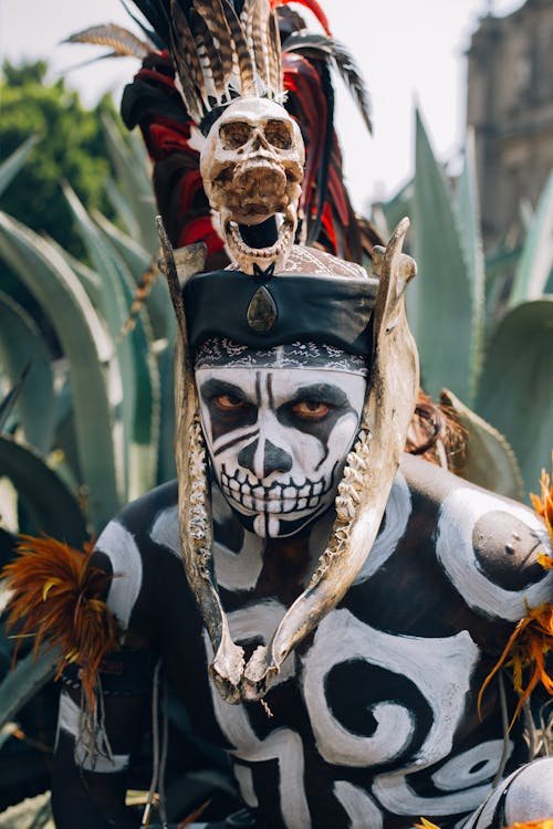 Native Mexican Aztec warrior, with pre-Hispanic makeup simulating a skull and a bone headdress adorned with feathers and cempazuchil flowers