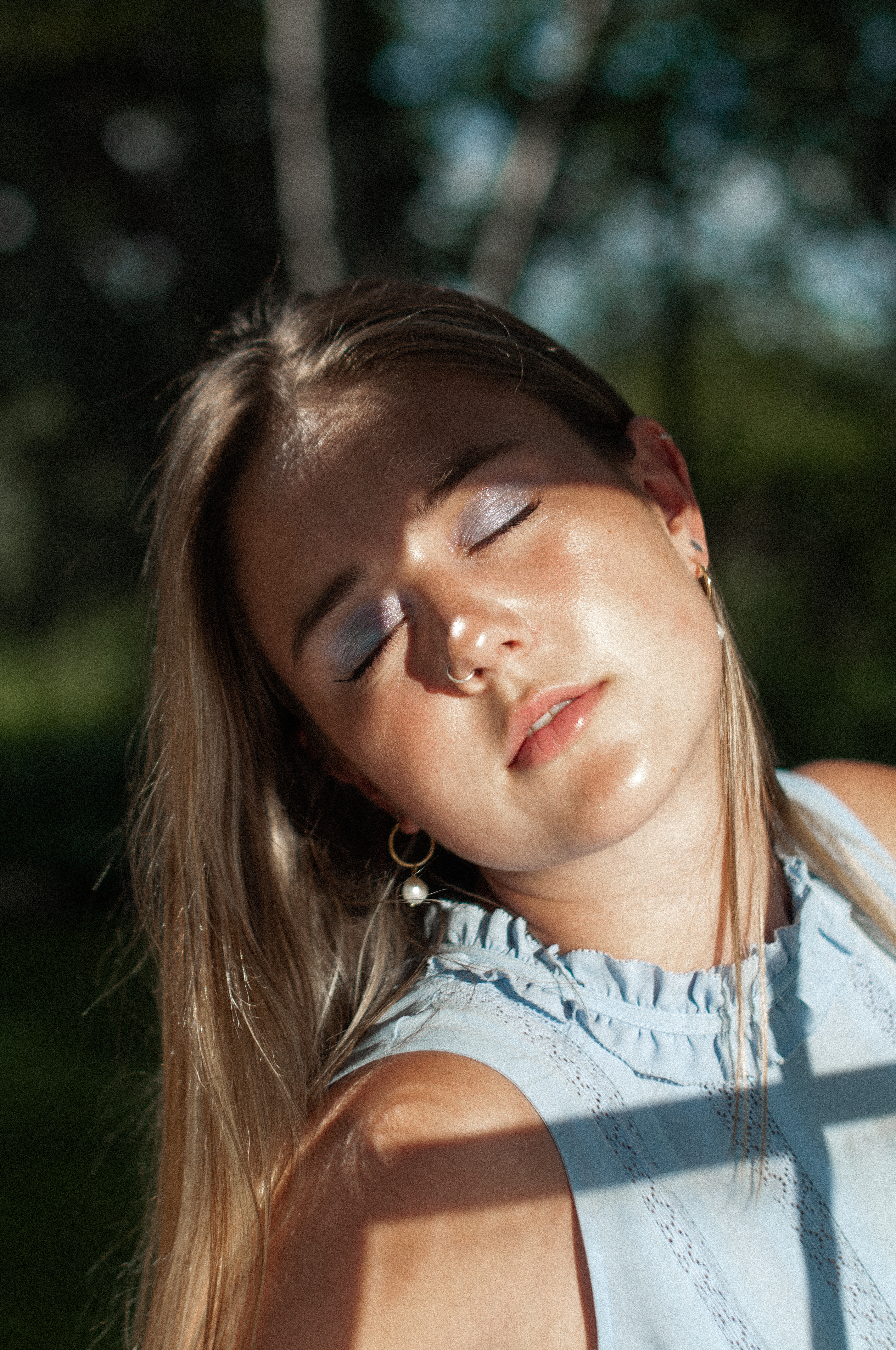 A peaceful close-up portrait of a woman with eyes closed, enjoying sunlight outdoors.