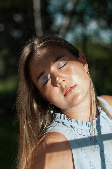 A peaceful close-up portrait of a woman with eyes closed, enjoying sunlight outdoors.