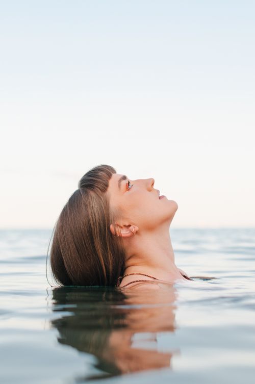 Free Profile view of woman enjoying a peaceful moment in the ocean, looking up at the sky. Stock Photo