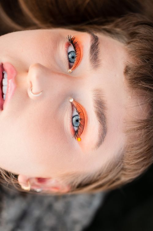 Free Artistic close-up of a woman with orange eyeshadow and gems, featuring blue eyes and nose piercing. Stock Photo
