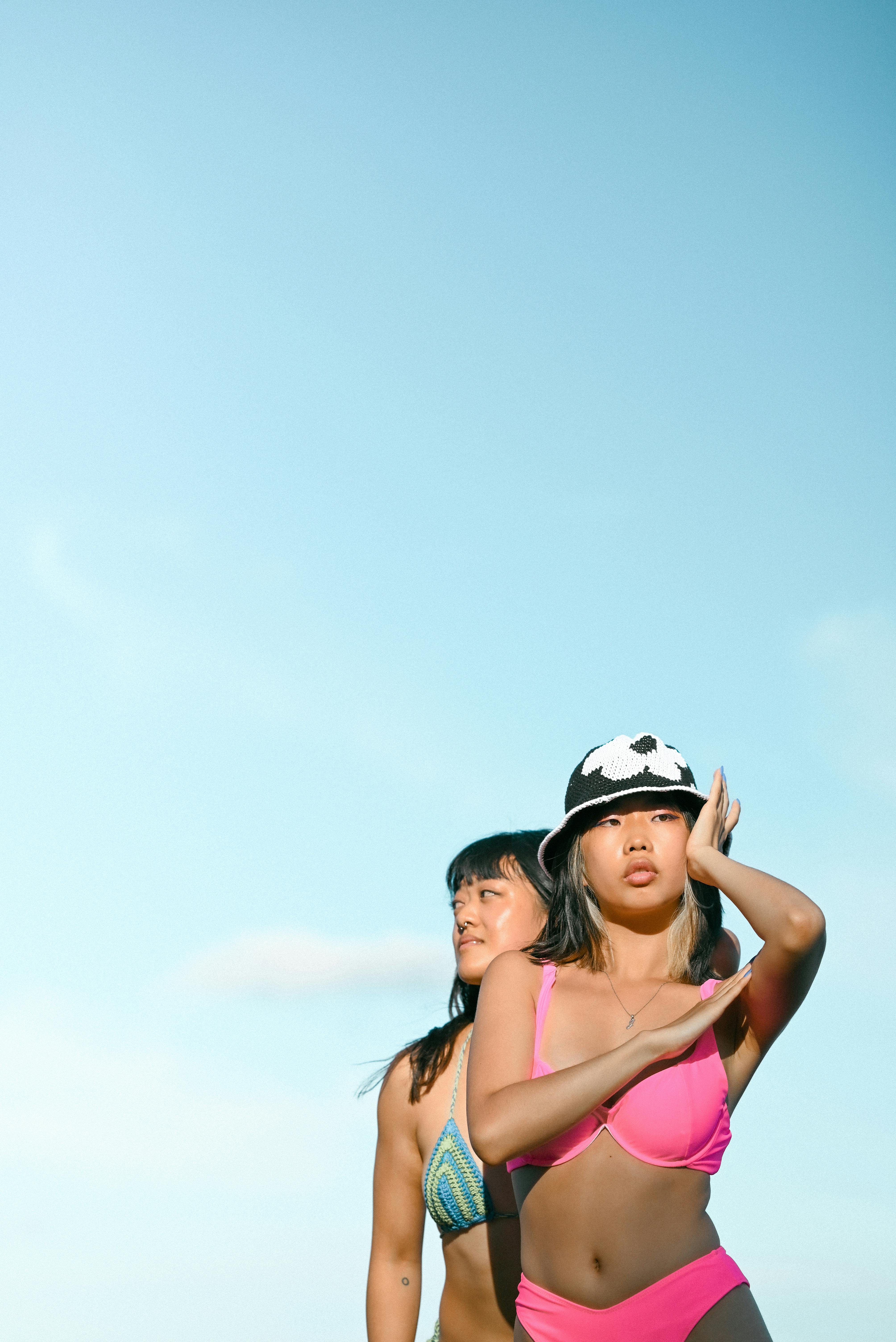 Two women in colorful bikinis posing outdoors with a bright blue sky background.