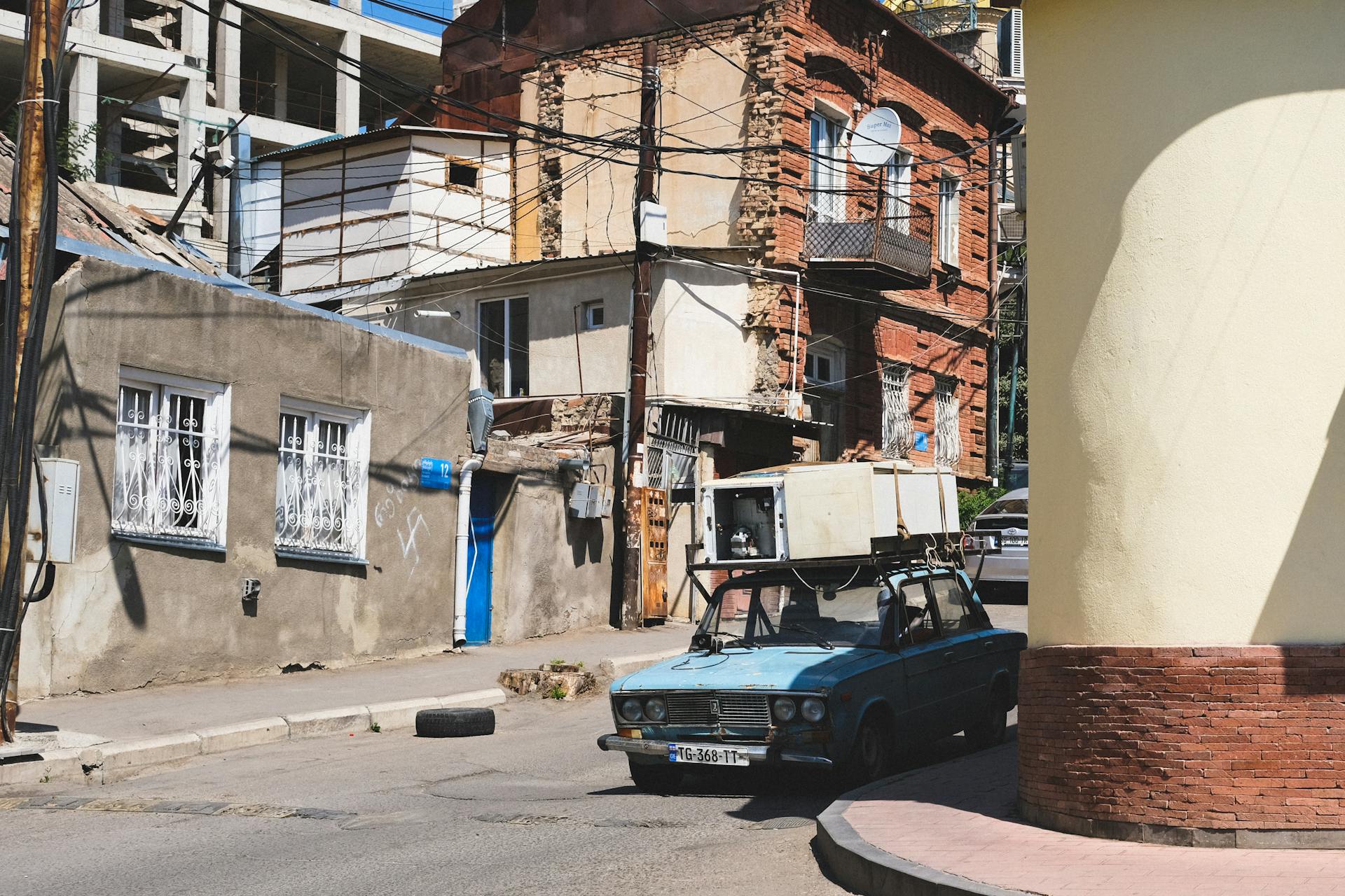 A vintage car drives through the rustic streets of Tbilisi, highlighting historic Georgian architecture.