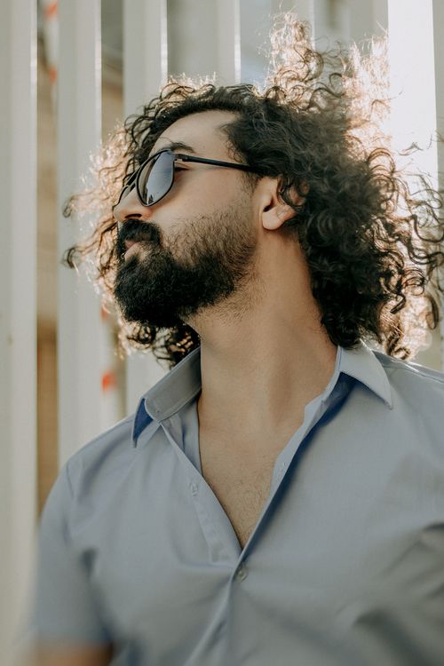 Free Stylish man with curly hair and sunglasses in a relaxed outdoor setting. Stock Photo