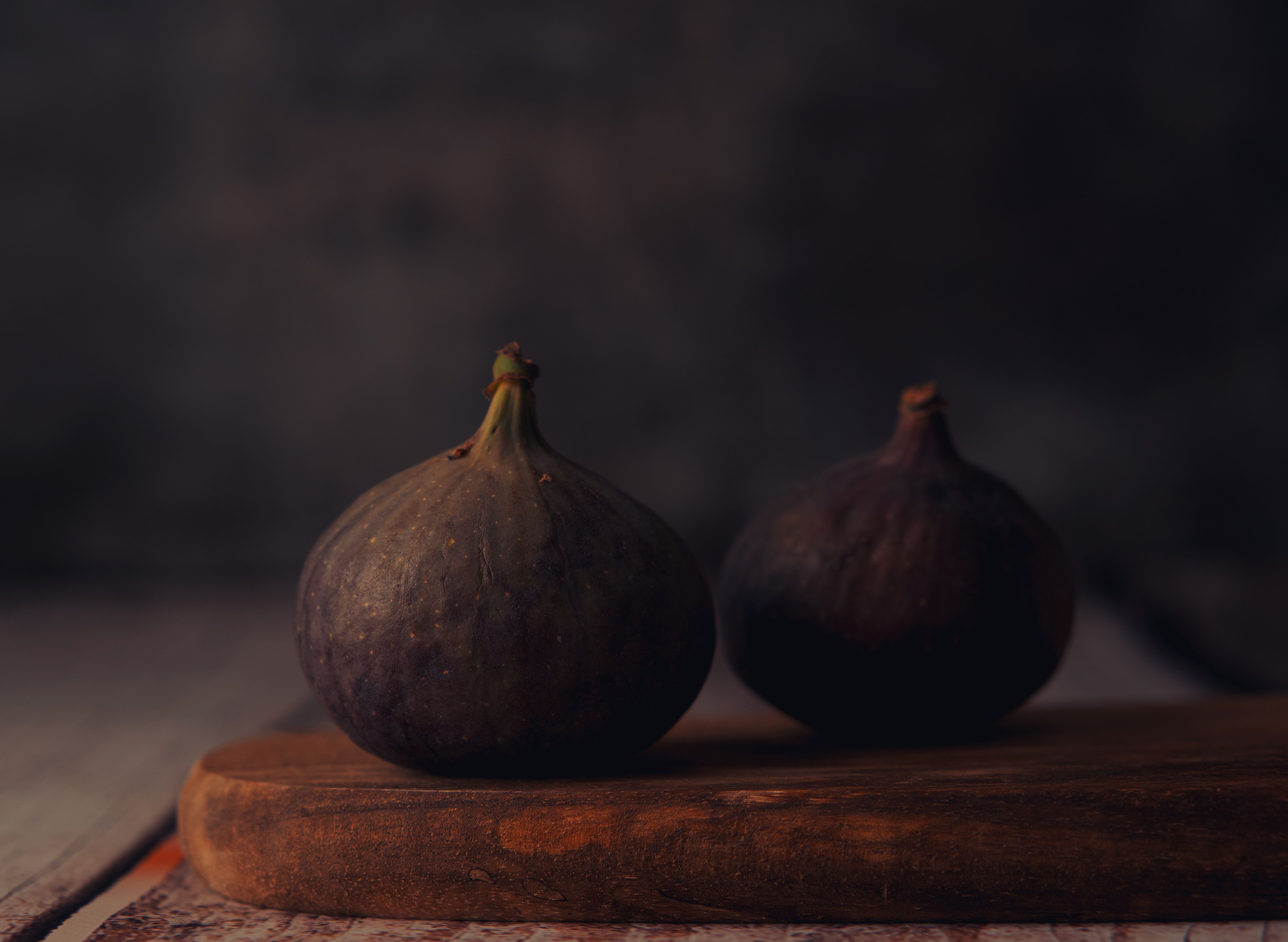 Close-up of two fresh figs resting on a rustic wooden board with a dark moody background.