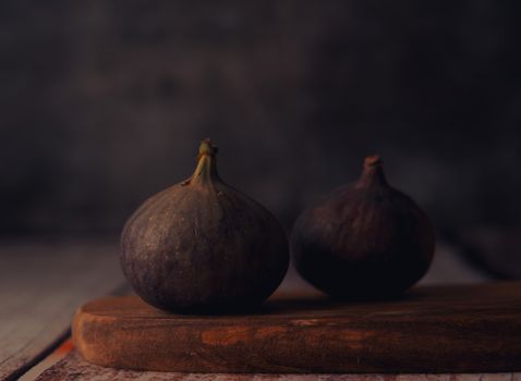 Close-up of two fresh figs resting on a rustic wooden board with a dark moody background.