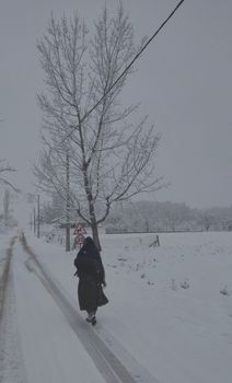 A person walks down a snow-covered rural road under grey skies in winter.