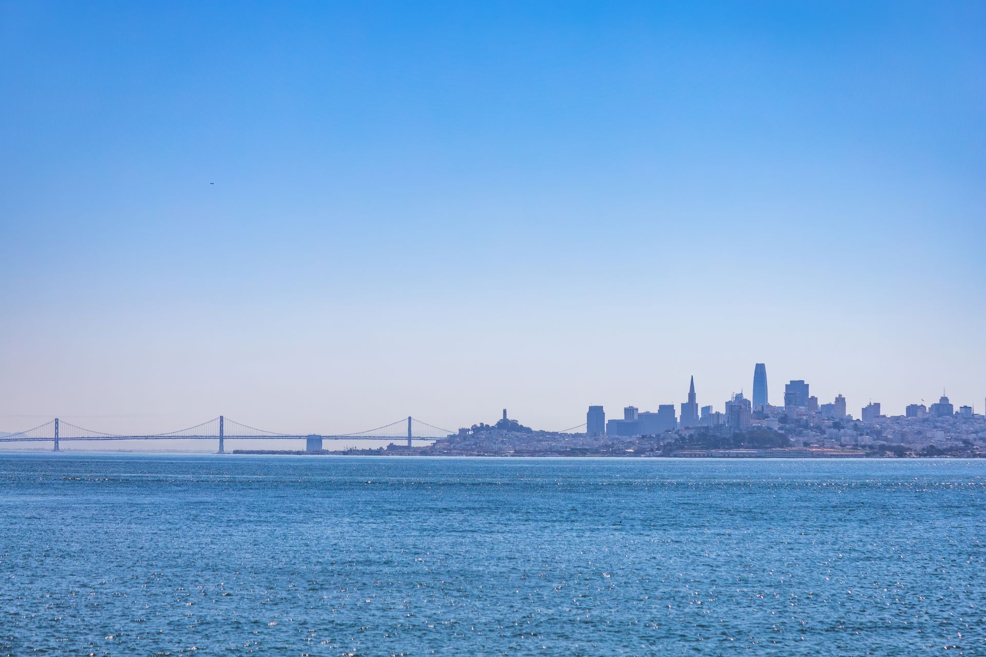 San Francisco skyline and Bay Bridge viewed across bright blue water under clear sky