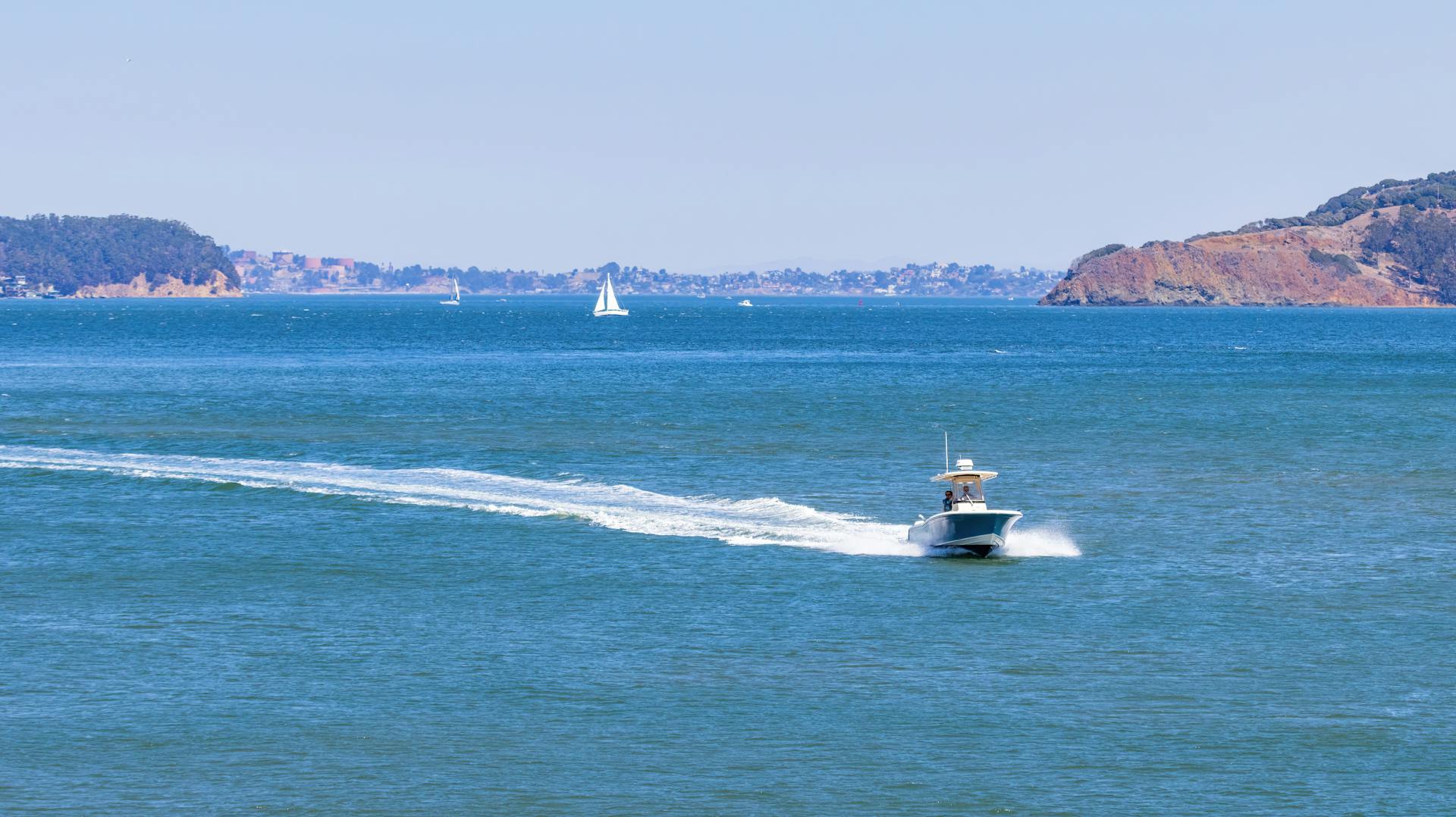 A speedboat navigates the blue ocean under clear skies, leaving a white wake behind.