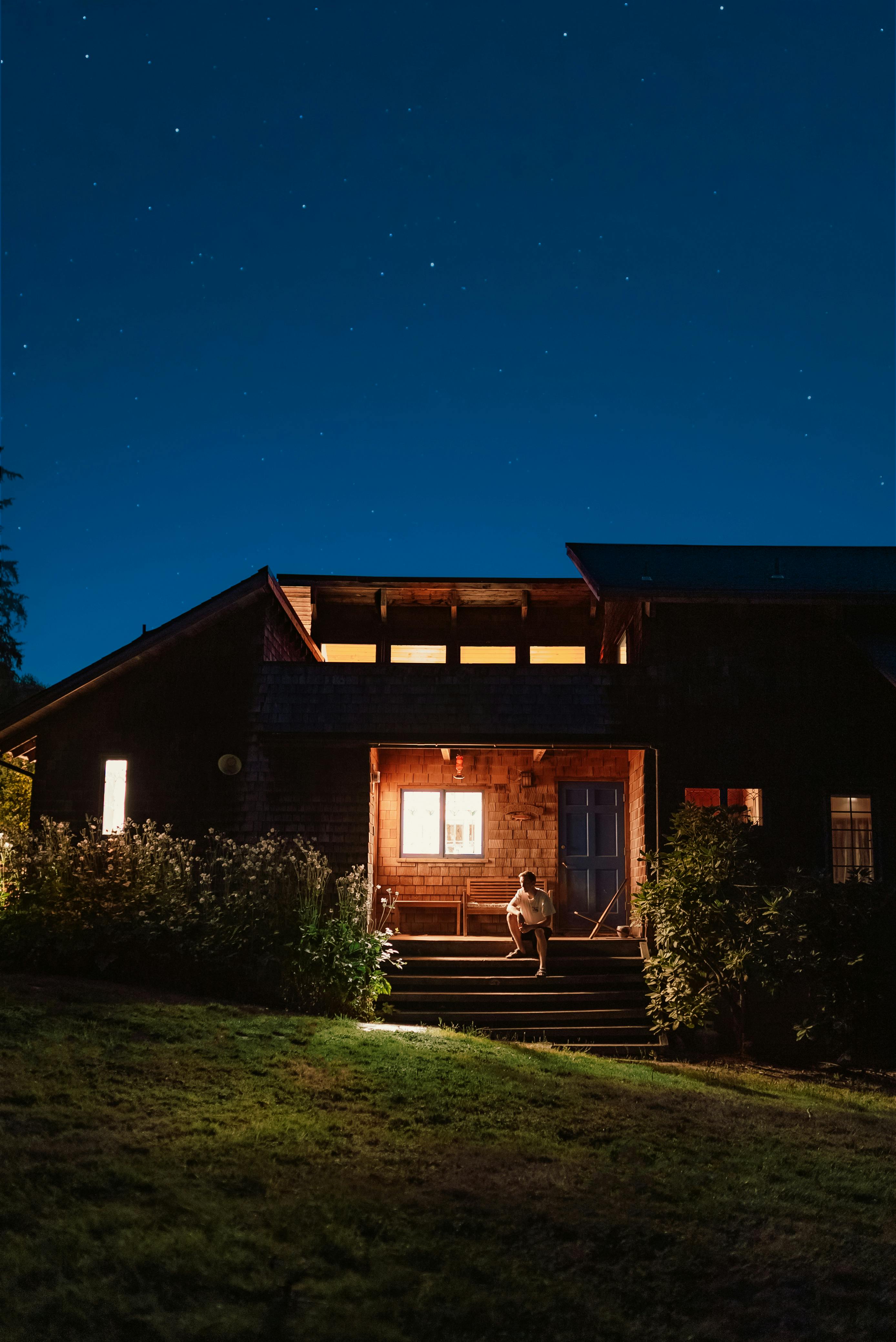 A person sitting on cabin steps, enjoying the starry night sky and serene ambiance.