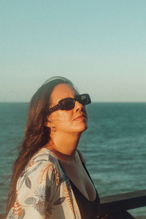 Free Woman enjoying a sunny day by the sea wearing sunglasses and a floral cover-up. Stock Photo