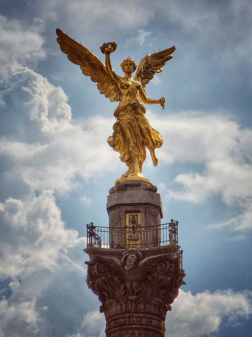 Free Glistening angel statue with wings spread wide atop a column, set against a backdrop of clouds. Stock Photo