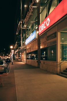 City street scene with illuminated signs including CIBC and LeGrow's Travel at night.
