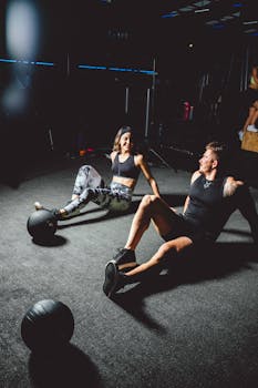 A man and woman sitting on the gym floor, smiling after a workout with medicine balls.