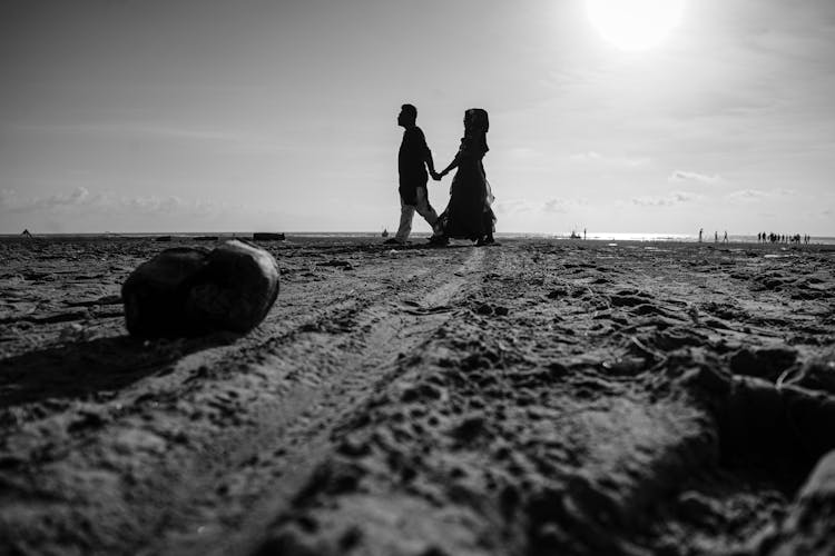 Black And White Photo Of Couple Walking At The Beach