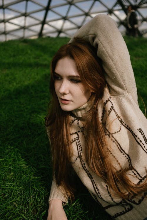 A Woman in Turtleneck Sweater Lying on Green Grass Field