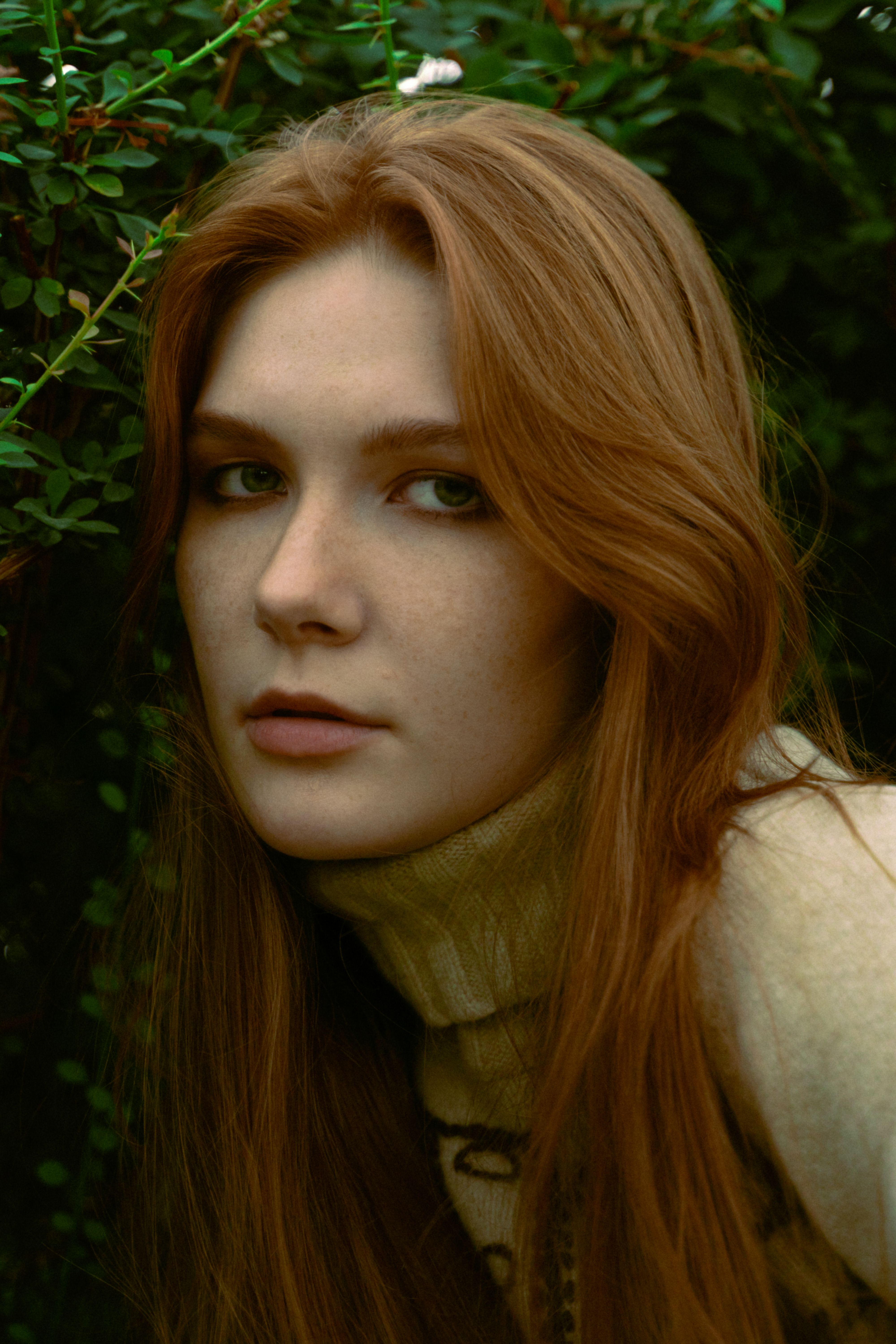 Portrait of a young redhead woman in a cozy turtleneck sweater surrounded by greenery.