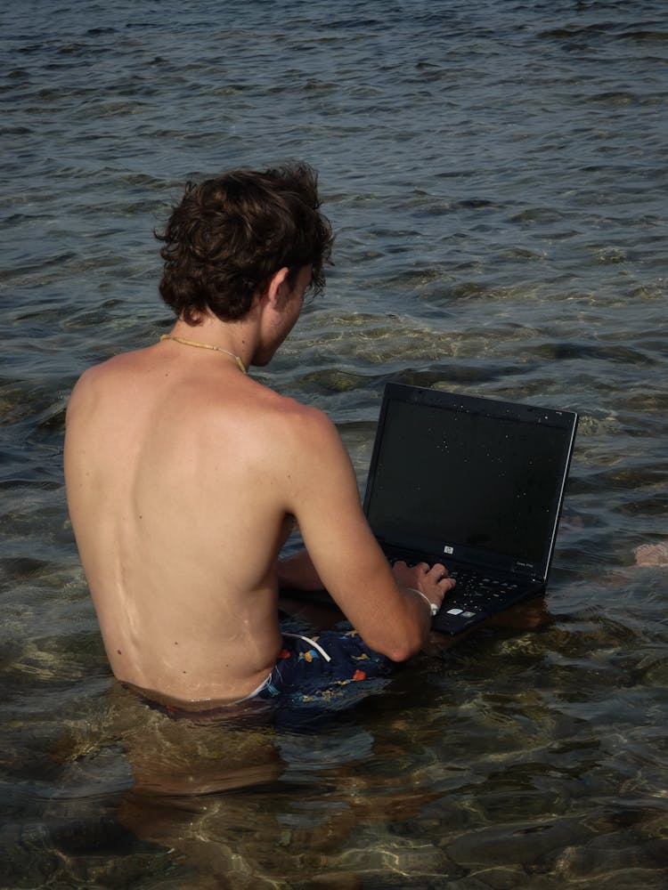 Man Sitting On Shallow Water Using A Laptop