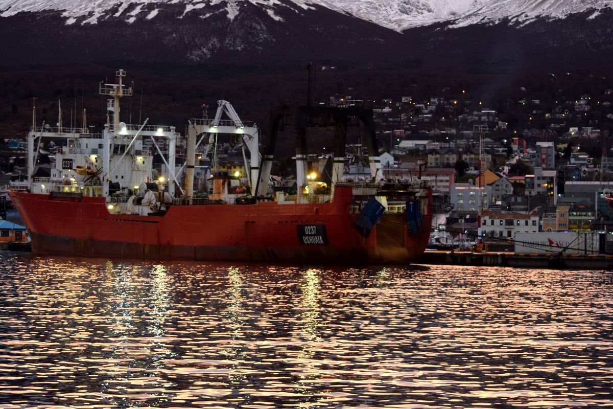 A large fishing vessel anchored at Ushuaia harbor during dusk with snowy mountains in the background.